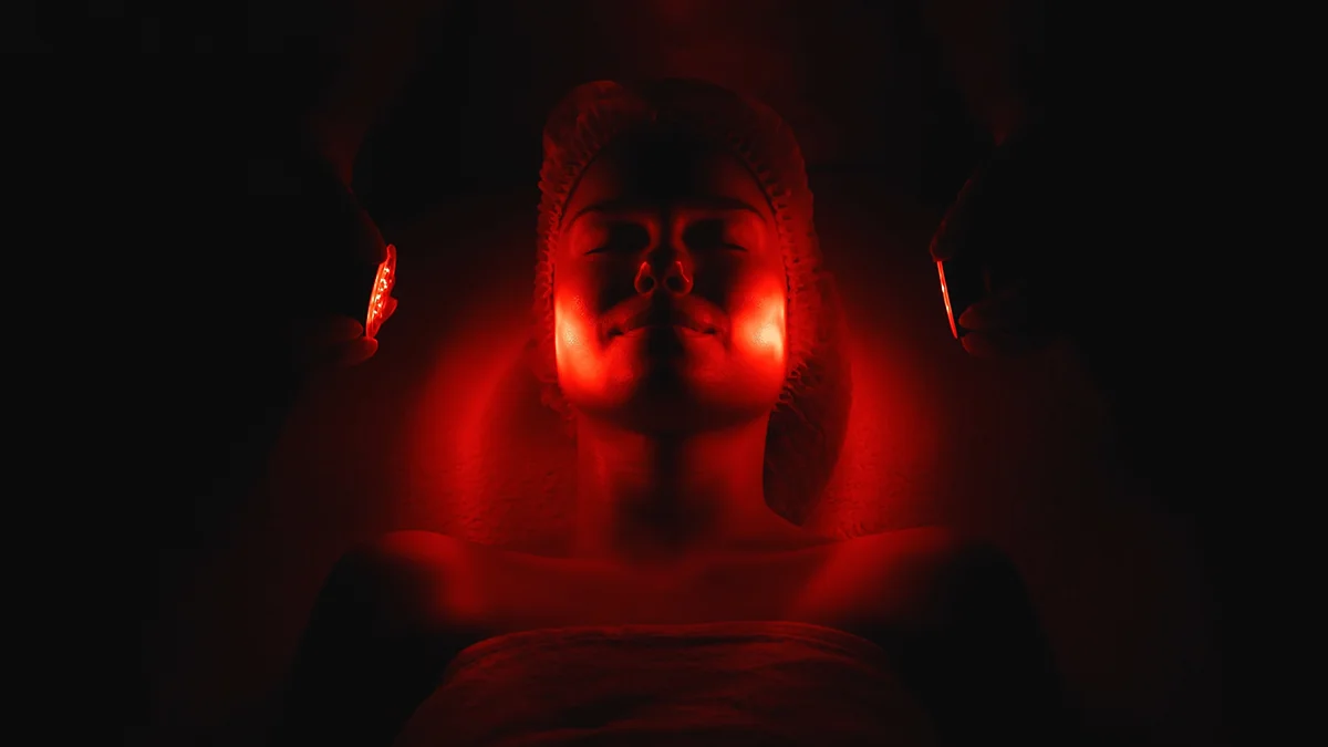 Content woman getting red light therapy for face in a dark room